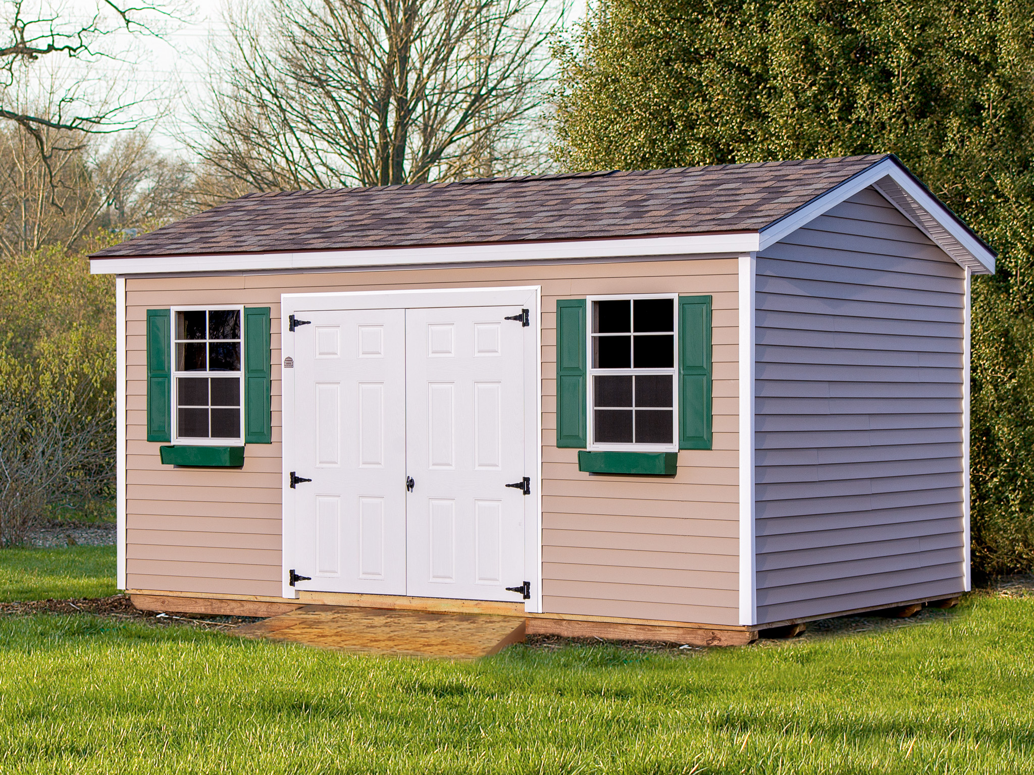 One of our garden sheds for sale in Owosso 2 MI - Beige siding with white double doors and windows with green shutters and window boxes beneath brown shingled roof
