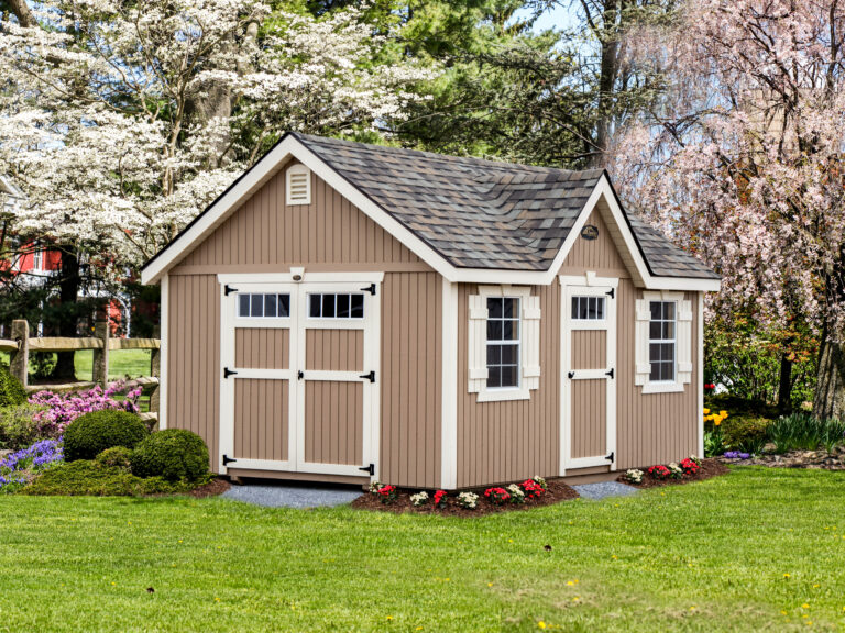 tan-colored cottage-style shed with white trim, double doors, and windows, flowering trees in background