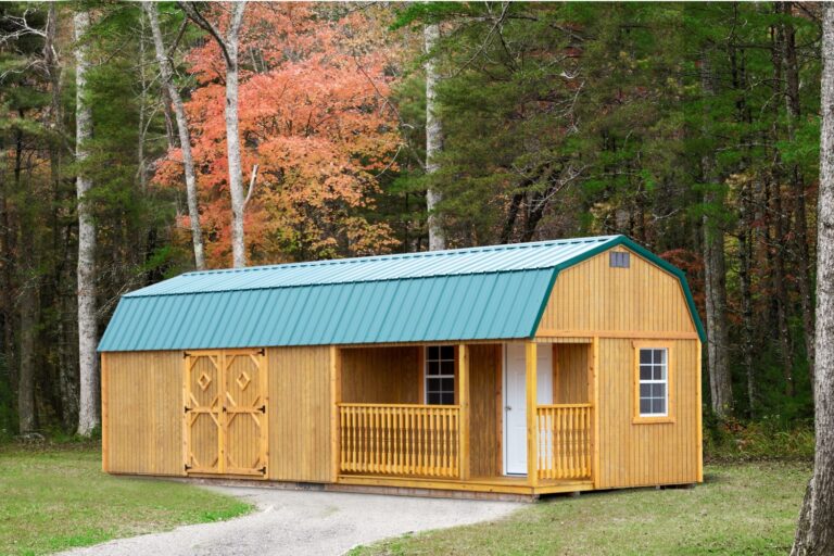 Wooden storage building with green roof and porch in a fall setting.